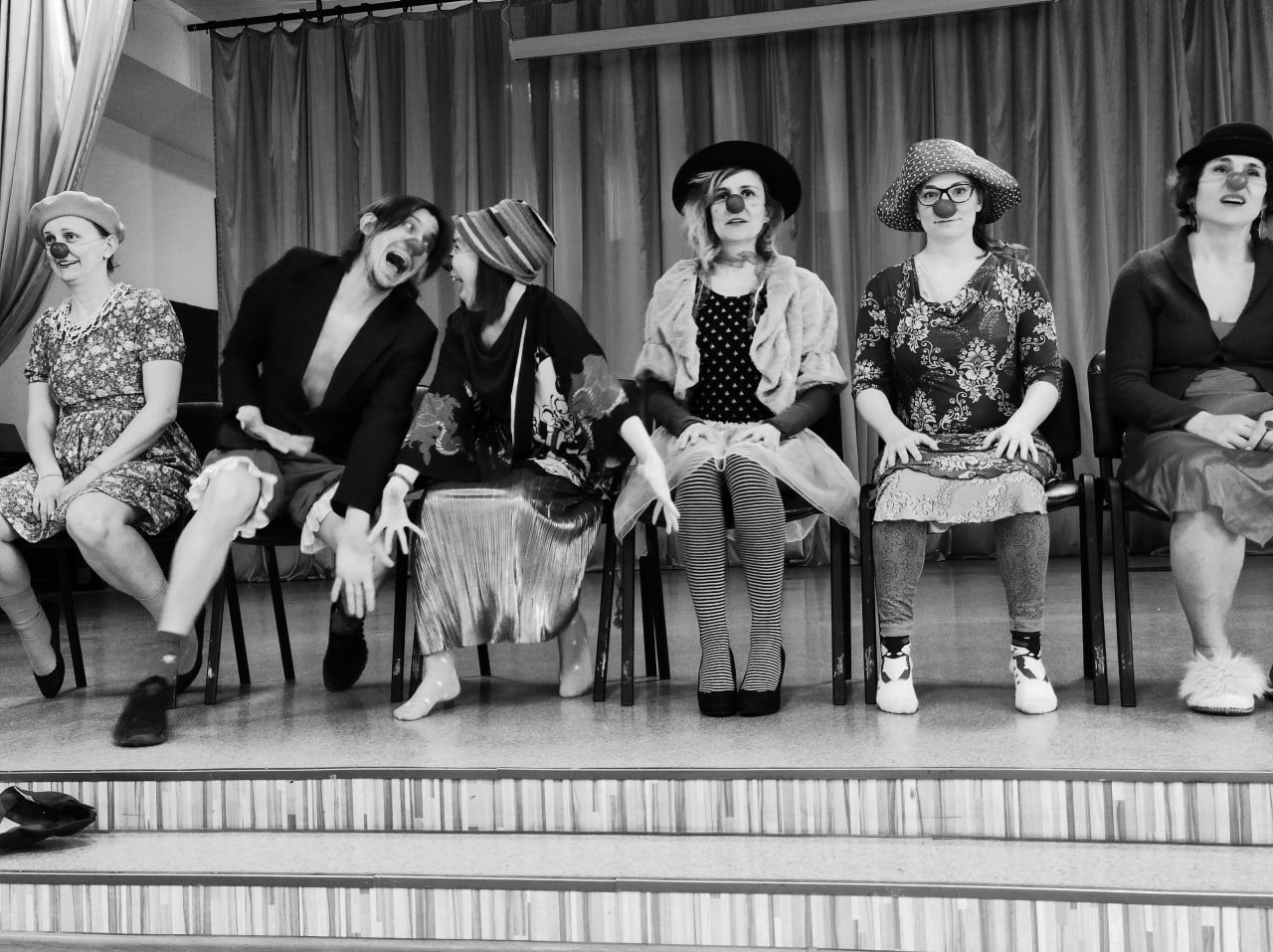 A row of clowns with red noses sitting on chairs on a stage