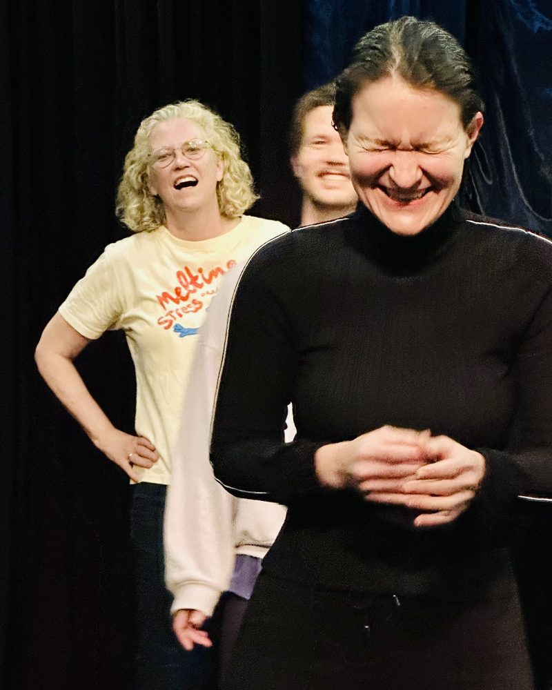 Two participants doubled over laughing against a black curtain