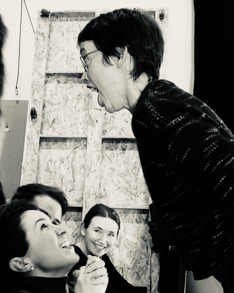 A participant leaning over two others and pulling a face, all three laughing