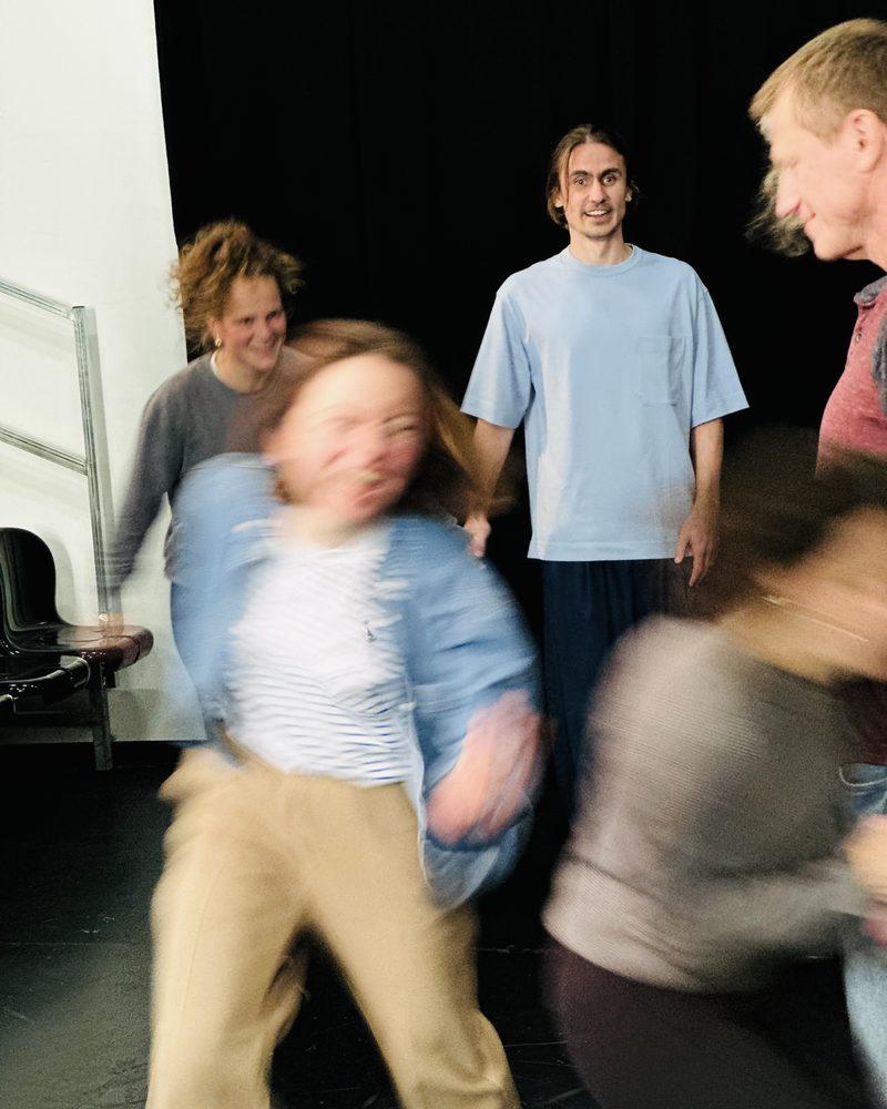 A participant crossing the room mid-movement, blurred, while the others watch